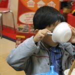 boy in gray zip up jacket drinking from white ceramic mug